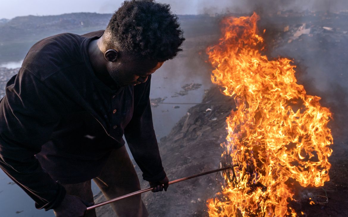 Old Fadama, Accra, Ghana, February 9, 2023. Simon Aniah, 24, burns scrap electrical cables to recover copper by the Korle Lagoon. © Muntaka Chasant for Fondation Carmignac Old Fadama, Accra, Ghana, February 9, 2023. Simon Aniah, 24, burns scrap electrical cables to recover copper by the Korle Lagoon. © Muntaka Chasant for Fondation Carmignac