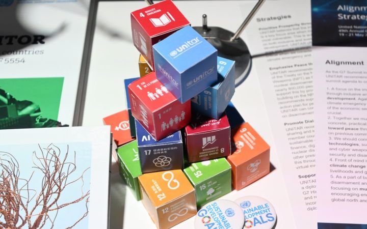 Piled collection of paper cubes featuring the SDG logos placed on a table with flyers and SDG pins.