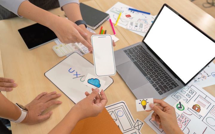 Hands of different people holding cutouts of their design ideas. A laptop can be seen on the right side of the frame.